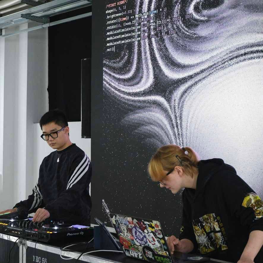 Two performers at a mixing desk before a projected visual