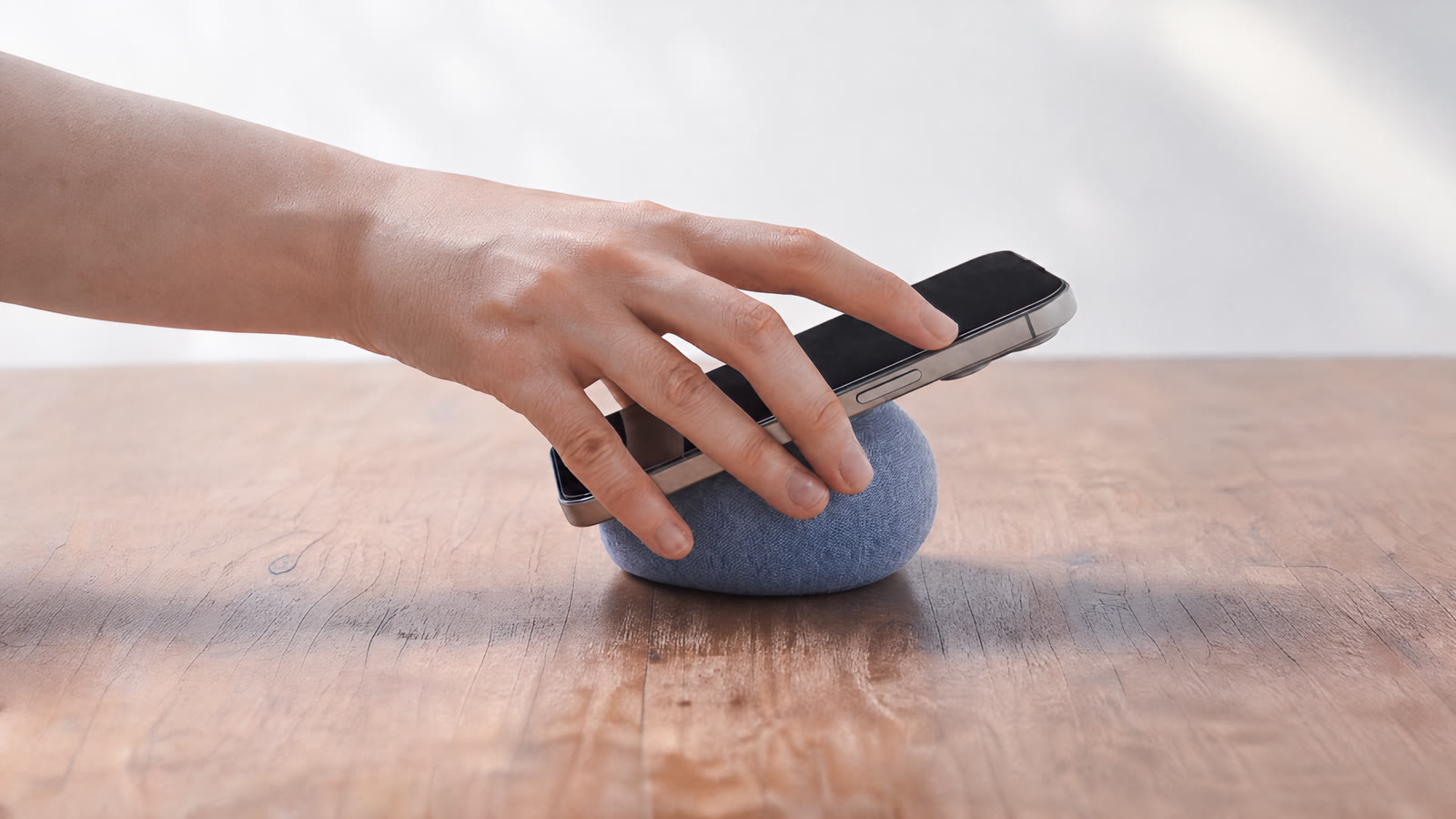 A hand setting a phone onto NEST on a wooden table